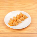 Plate of crispy pork gyoza, featuring golden-brown dumplings filled with savory pork, covered with a sauce at Kinton Ramen.